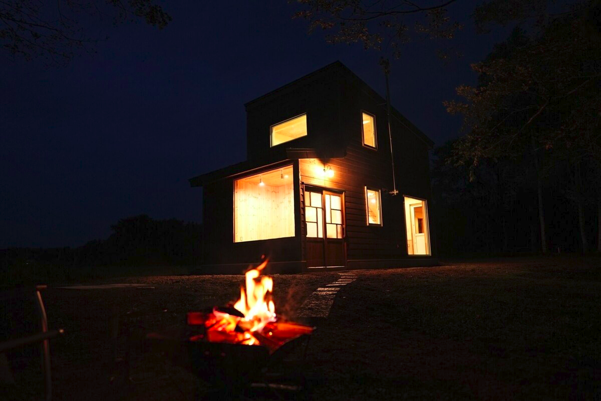 Square video example — a cabin lit up at night beside a campfire